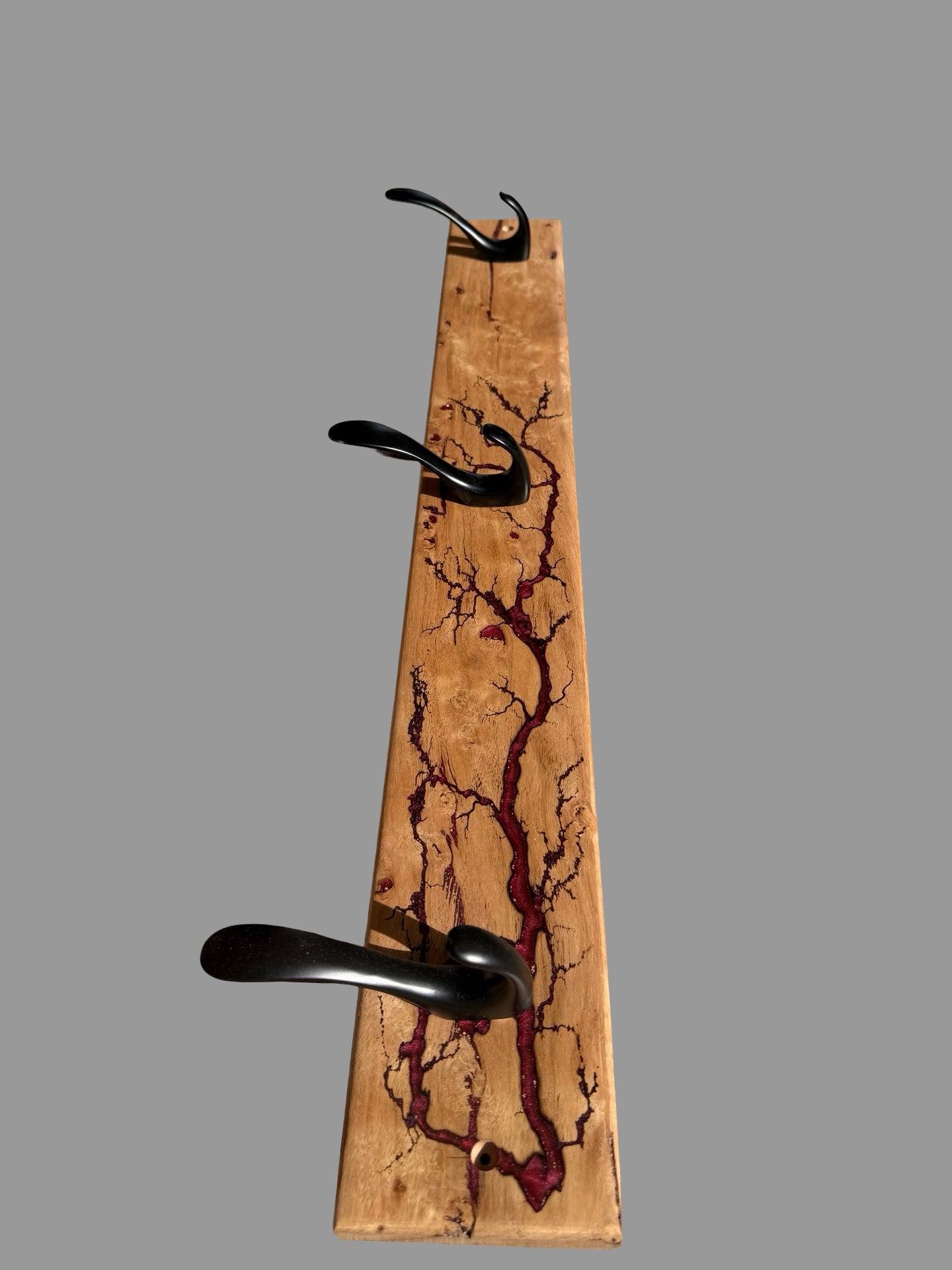 A rustic wall-mounted wooden coat rack with three black metal hooks, featuring a natural wood grain background with dark reddish-brown resin inlay in a tree-bark pattern, shown against a solid gray background.