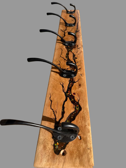 A rustic wooden coat rack with five black metal hooks, featuring a natural wood grain base with dark resin inlay in the shape of tree branches.