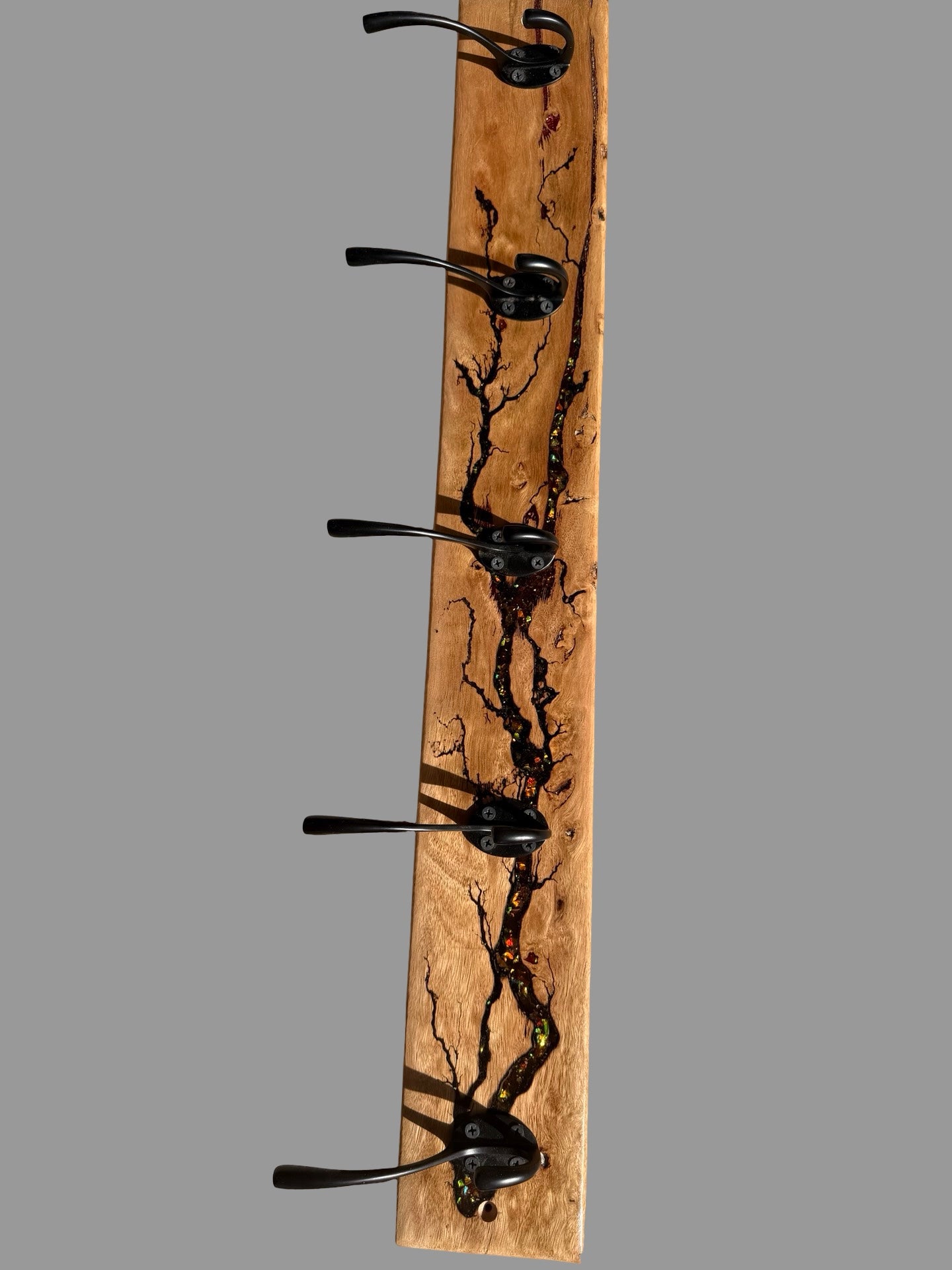 A rustic wooden coat rack with five black metal hooks, featuring a natural live-edge wood grain pattern with dark burn marks, shown against a solid gray background.
