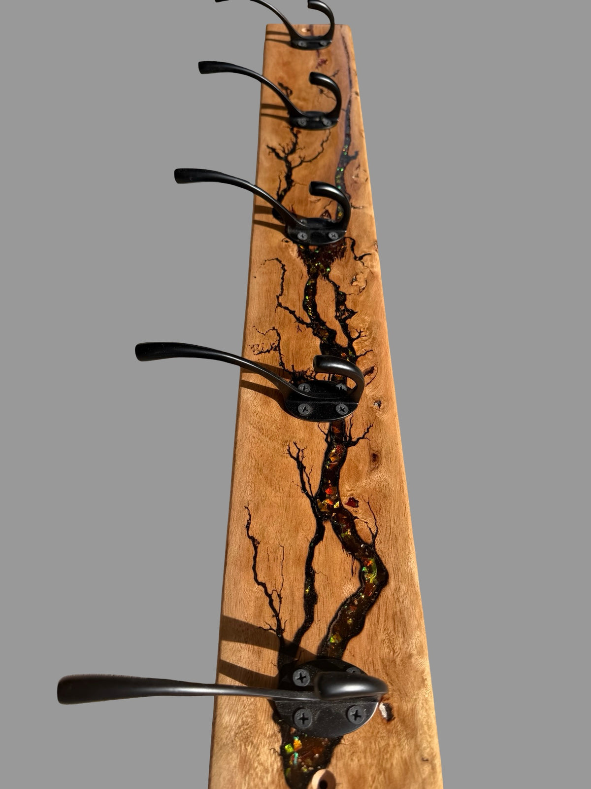 A rustic wooden coat rack with a natural prominent dark resin electric burn pattern and five black metal hooks.