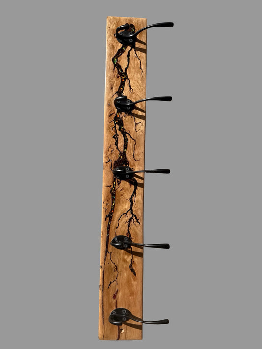 A rustic vertical wooden coat rack with five black metal hooks, featuring a natural live-edge wood grain pattern resembling tree branches, shown against a solid gray background.