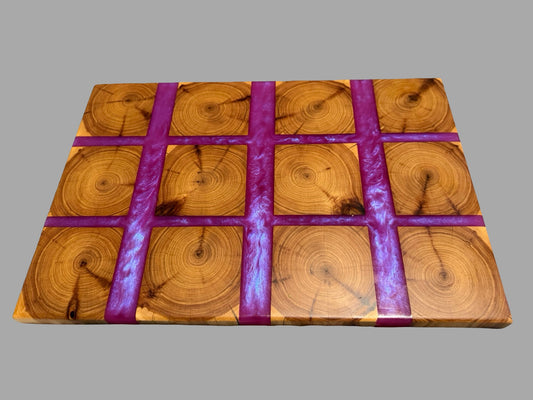 A rectangular wooden board with a grid pattern of circular wood slice designs and three vertical purple glittery stripes, shown on a solid gray background.