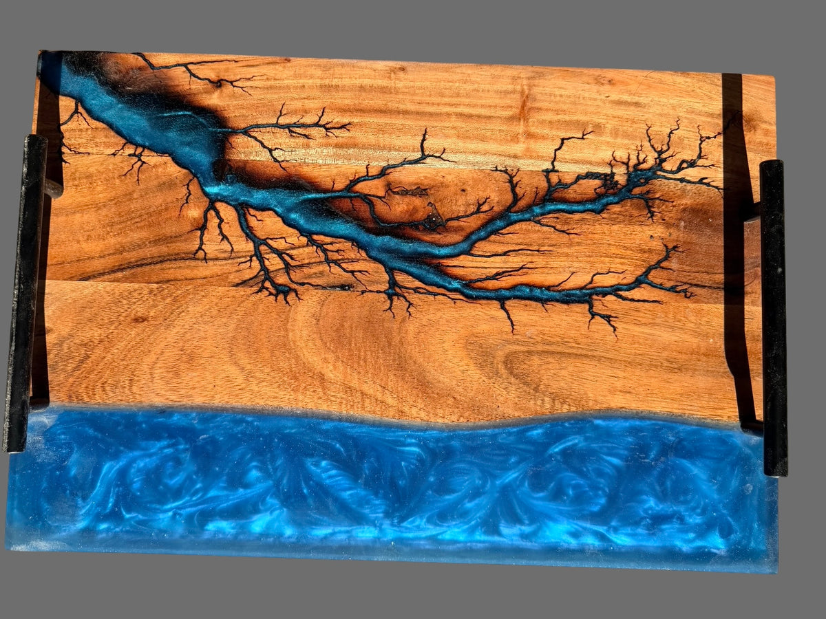Premium resin board  with black metal side handles, featuring acacia wood grain with a sapphire blue resin fractal burning pattern and a thick blue resin base layer, shown on a plain gray background. Great birthday gift for her or him